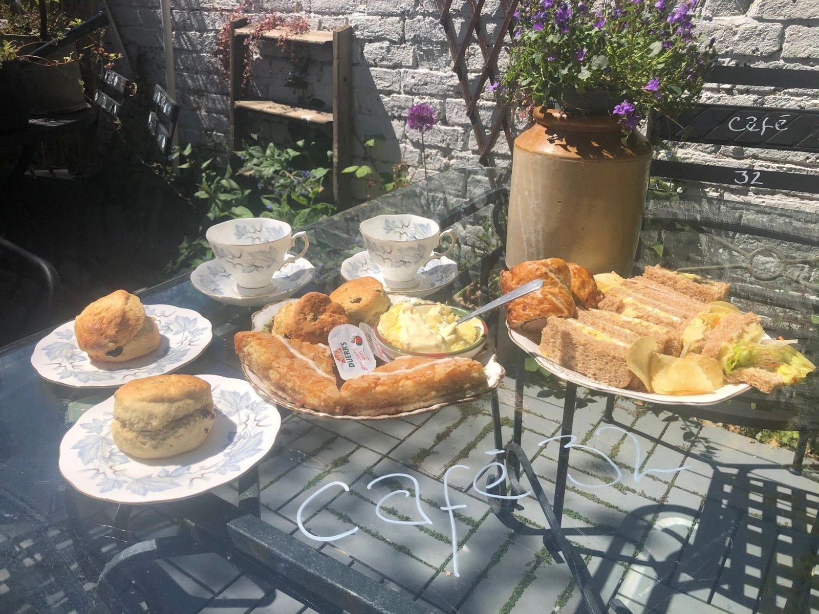 Afternoon tea in the sunshine: scones, sandwiches and pastries on doilies with china teacups